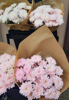 Beautiful gift bouquets of chrysanthemums in brown kraft paper, on the counter of a flower shop, vertical.