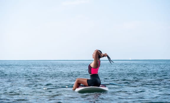 Silhouette of woman standing, surfing on SUP board, confident paddling through water surface. Idyllic sunset or sunrise. Sports active lifestyle at sea or river.