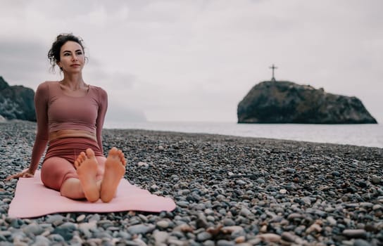 Middle aged well looking woman with black hair doing Pilates with the ring on the yoga mat near the sea on the pebble beach. Female fitness yoga concept. Healthy lifestyle, harmony and meditation.