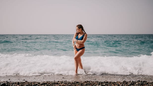 Beach vacation. Hot beautiful woman in sunhat and bikini standing with her arms raised to her head enjoying looking view of beach ocean on hot summer day.