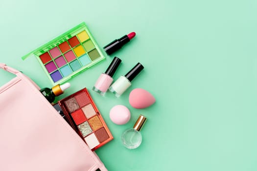 Bright summer eyeshadow palette and makeup products in pink cosmetic bag on green background. Makeup cosmetics. Colorful colors. Place for text. Flat lay. Top view. layout