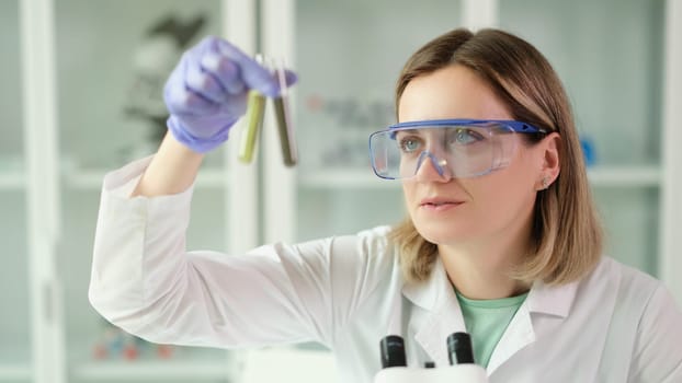 Woman chemist in protective glasses holding test tubes with liquid in hands in laboratory. Pharmaceutical business concept