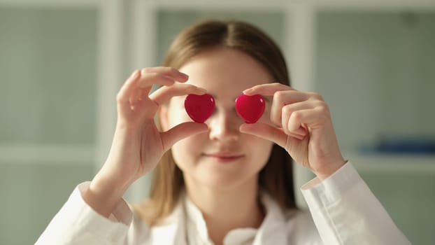 Doctor cardiologist holding two toy red hearts in front of eyes closeup. Cardiology medical care concept