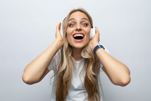 joyful young woman in white headphones listening to podcasts on white background.