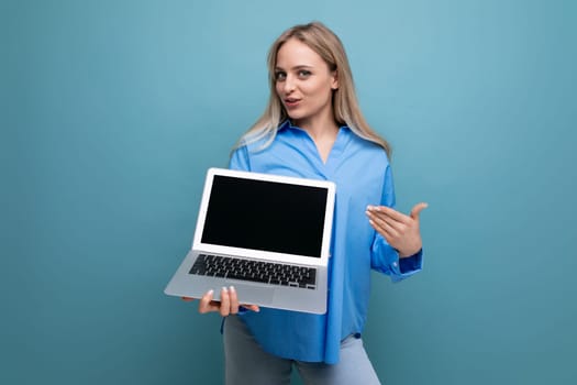smiling blonde girl with a laptop in her hands with an empty space for a web page on a blue background.
