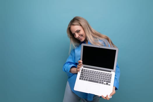 happy lucky blonde girl demonstrates laptop screen blank space for web page on blue background.