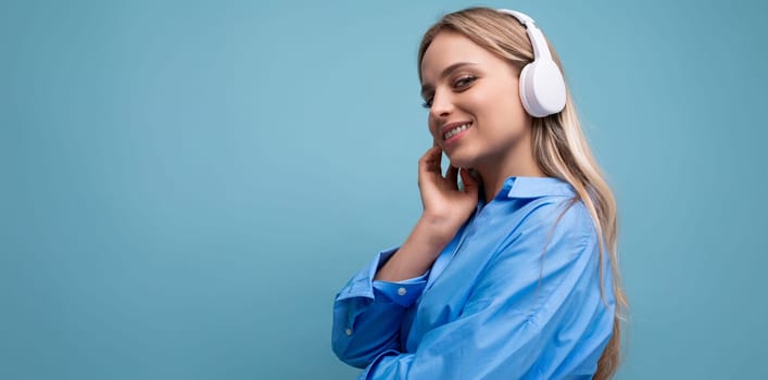 horizontal photo of an attractive girl in wireless large headphones listening with pleasure to music from a playlist on a blue background.