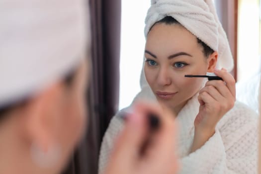 A woman applies black mascara to her eyelashes with a makeup brush. Young beautiful woman applying mascara makeup on her eyes in the bathroom.