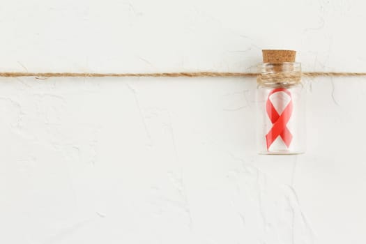 Red ribbon in a glass bottle with black notebook on white grunge background. Top view. Health care. AIDS prevention concept. Hiv and cancer awareness. Flat lay.