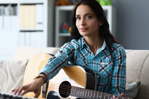 Talented young woman holding guitar in hands at home. Woman practicing playing musical chords concept