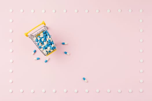 Supermarket trolley filled with capsules in a frame of pills on a pink background. Top view. Pharmacy concept.