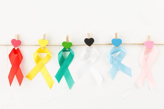 Colored ribbons on a rope with wooden clothespins with multicolored hearts against white background. Top view. Health care. AIDS prevention concept. Hiv and cancer awareness. Flat lay.
