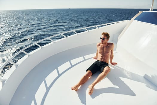 Warm weather. Young male tourist is on the yacht on the sea. Conception of vacation.