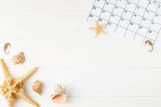 Summer vacation calendar at the sea on a white wooden background. Summer holiday concept. Decoration of starfish and seashells. Top view.