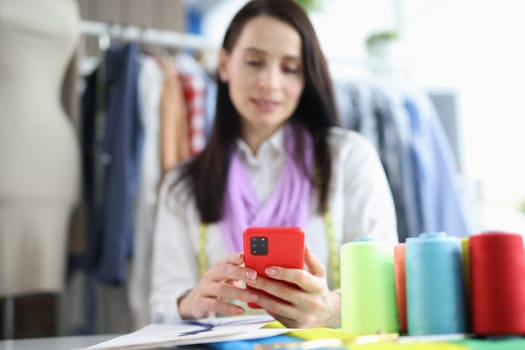 Woman seamstress stylist holding smartphone in atelier. Creative studio and accepting online orders through application