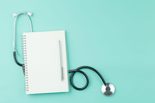 Open spiral notepad with black top pen view. Stethoscope on green medical background flat lay. Doctor or nurse desktop concept.