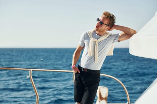 Warm weather. Young male tourist is on the yacht on the sea. Conception of vacation.