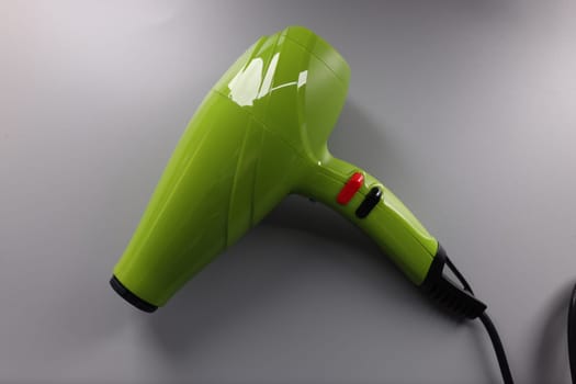 Green modern female hair dryer on gray background. Professional barber tool concept