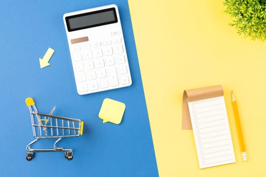 Supermarket trolley with calculator and shopping list. Discounts and promotions concept. Flat lay.