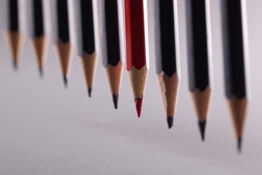 Red pencil stands out from crowd of many identical black pencils. Leadership career independence and strategy to think differently
