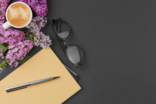 Spiral notebook with pen, glasses coffee cup and lilac flowers on an isolated background. Top view.