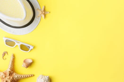Summer hat with sunglasses on yellow isolated background. Flat lay. Beach vacation concept. Top view. Starfish and seashells.