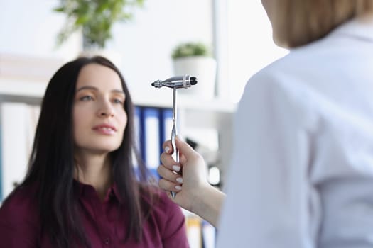 Neurologist checks reflexes with special hammer while examining young female patient in medical office. Vision pathology and neurological diseases concept