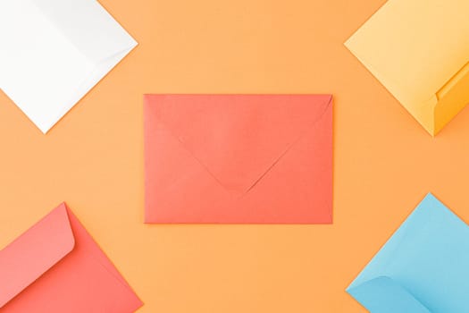 Multicolored paper mailing envelopes on orange isolated background. Top view, copy space.