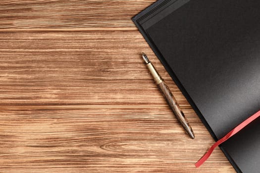 Open notebook with black sheets and a red bookmark gold with wood fountain pen on a light wooden background close up view.