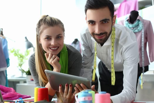 Smiling designer stylist discusses tailoring of new clothes with client and holds clipboard. Mobile apps for seamstress sketches