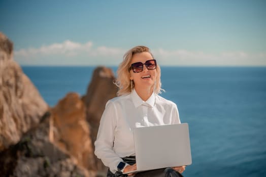 Business woman on nature in white shirt and black skirt. She works with an iPad in the open air with a beautiful view of the sea. The concept of remote work