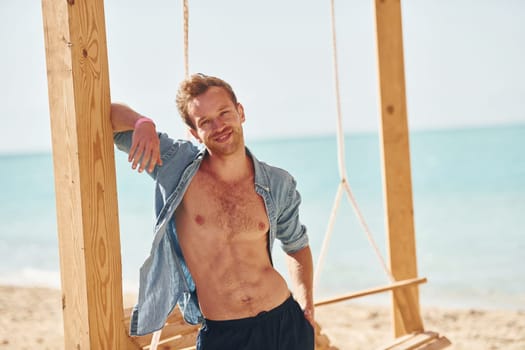 Shows body. Young european man have vacation and enjoying free time on the beach of sea.