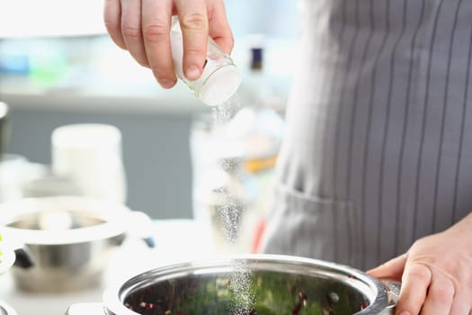 Cook pours salt into pan in kitchen. Dosage of salt in dishes concept