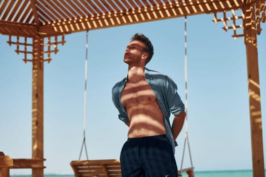 Shows body. Young european man have vacation and enjoying free time on the beach of sea.