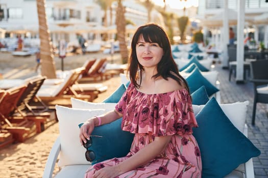 Sitting on the chair. Happy mature woman is outdoors enjoying her vacation at sunny daytime.