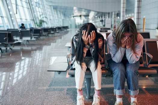 Sad young girl crying with her friend when sitting in the modern airport.
