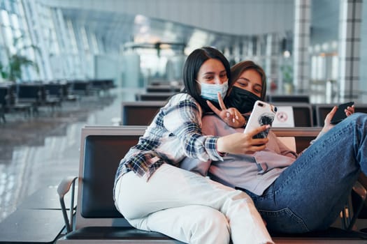 Two happy female friends taking selfie in the modern airport.