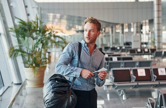 Young man in formal wear is in modern airport. Conception of vacation.