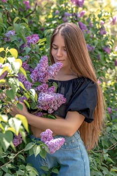 portrait of young woman with long hair outdoors in blooming lilac garden.