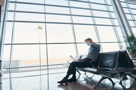 Sitting inside. Young man in formal wear is in modern airport. Conception of vacation.