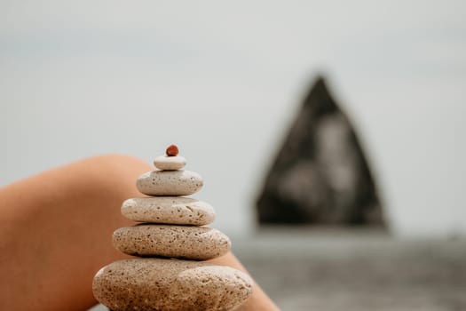 Woman bilds stones pyramid on the seashore on a sunny day on the blue sea background. Happy holidays. Pebble beach, calm sea, travel destination. Concept of happy vacation on the sea, meditation, spa