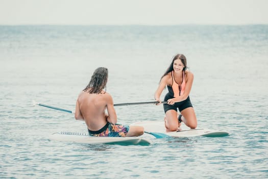 Sea woman and man on sup. Silhouette of happy young woman and man, surfing on SUP board, confident paddling through water surface. Idyllic sunset. Active lifestyle at sea or river