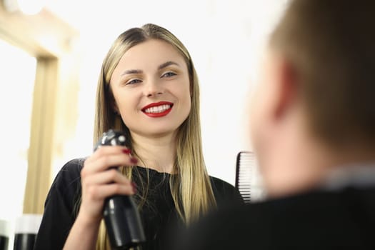 Smiling female hairdresser communicates with man in beauty salon. Choice of fashionable stylish male hairstyle concept