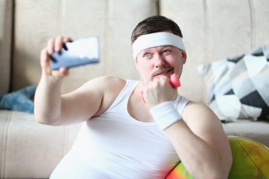 Young man takes selfie with dumbbells in hands. Sports blogger and home fitness concept