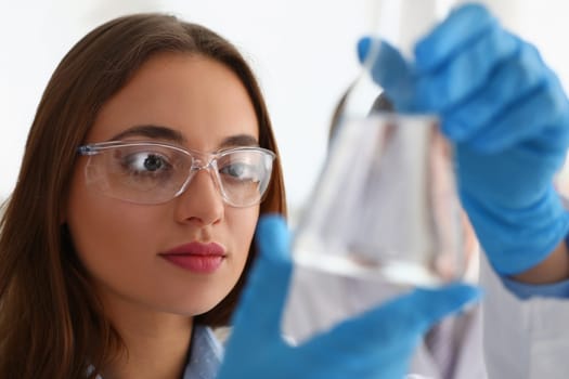 Portrait of woman scientist in glasses holds flask with transparent liquid. Laboratory study of water concept