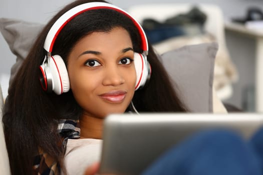 Smiling african american woman in headphones with laptop sitting on sofa at home. Listening to music or watching movies concept