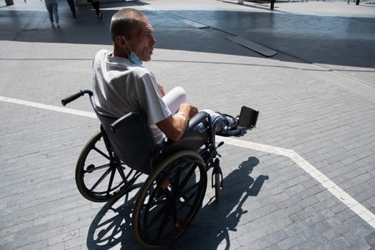 middle-aged man with a broken leg in a cast in a wheelchair on a walk near the hospital. High quality photo