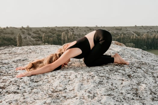Well looking middle aged woman with long hair, fitness instructor in leggings and tops doing stretching and pilates on the rock near forest. Female fitness yoga routine concept. Healthy lifestyle.