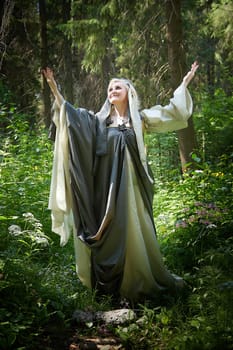 Adult mature woman 40-60 in a green long fairy dress in forest. Photo shoot in style of dryad and queen of nature. Fairy in beautiful green summer forest. Concept of caring for nature