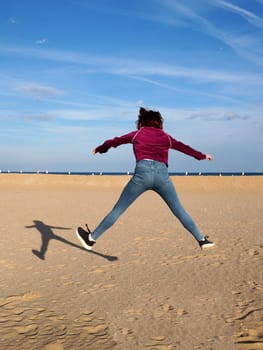 red-haired teen girl jumping with her arms and legs outstretched, rear view.